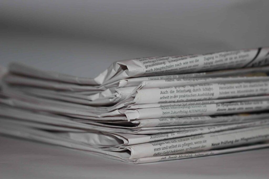 A stack of folded newspapers, slightly crumpled, lies on a surface with text written in German. The simple, neutral background highlights the texture and layers of the papers, evoking stories from bustling city streets and perhaps even developments in social housing. ©Mobysoft