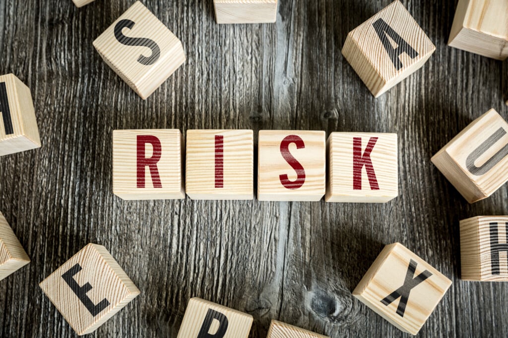 Wooden blocks spelling "RISK" are arranged in the center on a rustic wooden surface, symbolizing risk likelihood. Other scattered blocks with different letters surround them, creating a dynamic composition. ©Mobysoft