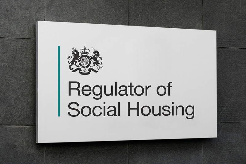 A sign reads "Regulator of Social Housing," with a government emblem above the text, mounted on a dark wall, reflecting Tenant Satisfaction Measures. ©Mobysoft