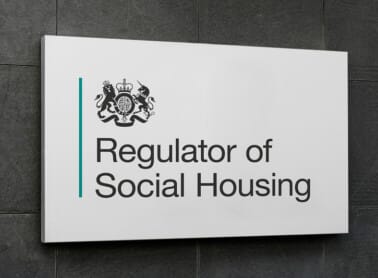 A sign reads "Regulator of Social Housing," with a government emblem above the text, mounted on a dark wall, reflecting Tenant Satisfaction Measures. ©Mobysoft
