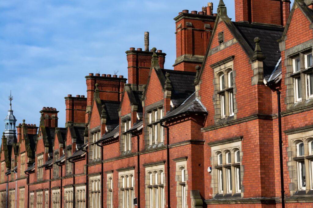 A row of red brick Victorian-style terraced houses with ornate chimneys and peaked roofs under a clear blue sky. The buildings feature cream-colored stone accents around the windows. ©Mobysoft