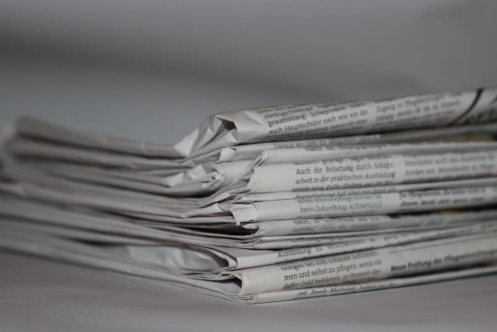 A stack of folded newspapers rests on a plain surface, their slightly crumpled edges revealing bold text in a foreign language. The close-up image highlights layered pages, possibly hinting at social housing news woven into the stories within. ©Mobysoft