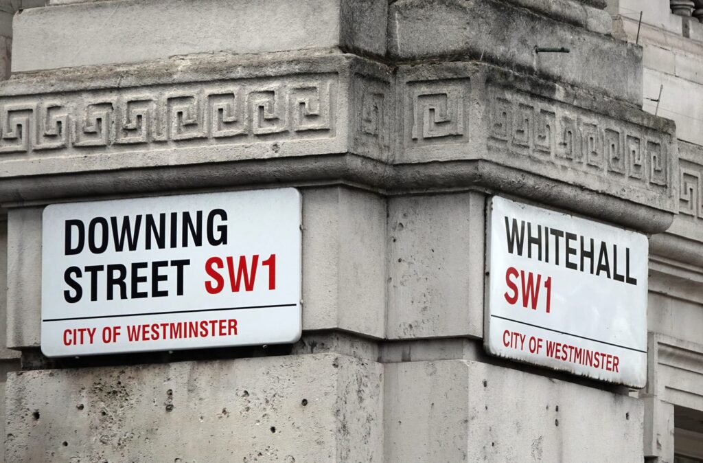 A corner of a stone building displays two street signs: "Downing Street SW1" and "Whitehall SW1," both in the City of Westminster, where crucial discussions on Housing 2024 are expected to shape the future. The signs are white with red and black text. ©Mobysoft