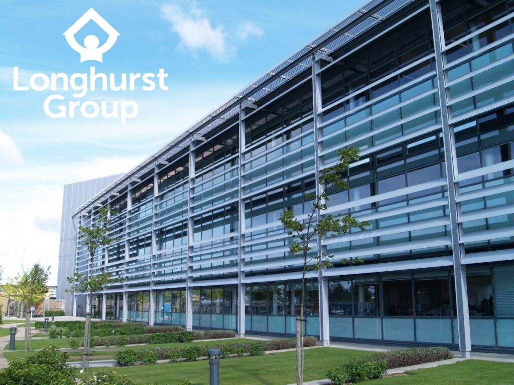 Modern office building with large glass windows and a grid-like facade. "Longhurst Group" logo is visible in the top left corner. The foreground features a well-maintained lawn with young trees and small shrubs under a partly cloudy sky. ©Mobysoft