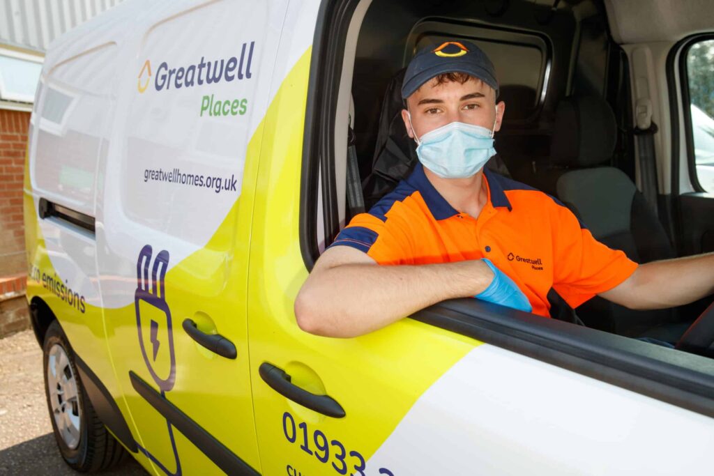 A delivery person in an orange uniform, cap, and face mask sits in a white and yellow "Greatwell Places" van. With their elbow resting on the window frame, they seem ready to tackle any task—be it delivering parcels or addressing damp and mould issues with efficiency. ©Mobysoft