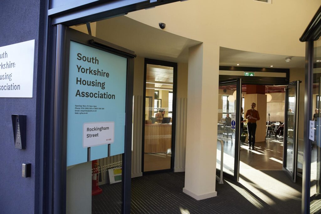 Entrance to South Yorkshire Housing Association at Rockingham Street features open glass doors with a person standing inside. The modern interior, reminiscent of Stirling Council's contemporary designs, is bathed in natural lighting. ©Mobysoft